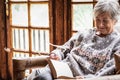 Portrait of senior woman sitting at home on armchair reading a book wearing a warm sweater and eyeglasses. Comfortable living room Royalty Free Stock Photo