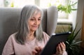 Portrait of senior woman sitting indoors on sofa at home, using tablet. Royalty Free Stock Photo