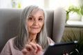 Portrait of senior woman sitting indoors on sofa at home, using tablet. Royalty Free Stock Photo