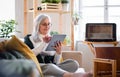 Portrait of senior woman sitting indoors on sofa at home, using tablet. Royalty Free Stock Photo