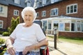 Portrait Of Senior Woman Sitting Outside Retirement Home In Motorized Wheelchair