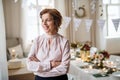 A portrait of a senior woman standing indoors in a room set for a party.