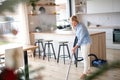 Portrait of senior woman with vacuum cleaner indoors at home, hoovering.