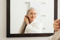 Portrait of a senior woman with a wood comb looking at a mirror. Aged female combing her beautiful long grey hair Royalty Free Stock Photo