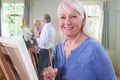 Portrait Of Senior Woman Attending Painting Class With Teacher In Background Royalty Free Stock Photo