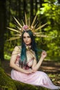 Portrait of Sensual Caucasian Girl with Artistic Flowery Golden Crown Posing in Empty Summer Forest Against High Trees