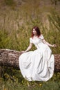 Portrait of Sensual Redhaired Girl in White Dress Outdoors. Posing on Wood Pile Against Sun