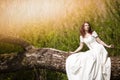 Portrait of Sensual Redhaired Girl in White Dress Outdoors. Posing on Wood Pile Against Sunlight