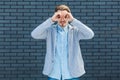 Portrait of serious attentive handsome young blonde man in casual style standing with binoculars gesture hand on eyes and looking Royalty Free Stock Photo