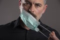 Portrait of serious attitude man taking off medical protection mask over gray studio background. Concept of personal