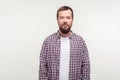 Portrait of serious bearded young man in plaid shirt standing looking at camera with calm confident attentive expression. white