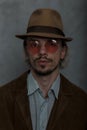 Portrait of a serious bearded young man in vintage red glasses in an elegant hat in a fashionable brown jacket in a classic Royalty Free Stock Photo