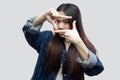 Portrait of serious beautiful brunette asian young woman in blue denim jacket with makeup standing and looking at camera with crop