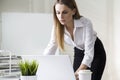 Portrait of a serious and beautiful businesswoman standing near her desk and working with her laptop. Royalty Free Stock Photo