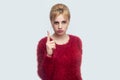 Portrait of serious beautiful young blond woman in red blouse standing and looking at camera with warning finger and alarming Royalty Free Stock Photo