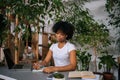 Portrait of serious black female freelancer in headphones writing notes, watching webinar, reading paper book studying Royalty Free Stock Photo