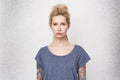 Portrait of serious blonde girl wearing blue t-shirt, tattoed arms and pierced nose sad and confused. She lost her boyfriend Royalty Free Stock Photo