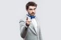 Portrait of serious bossy handsome bearded man in casual grey suit and blue bow tie standing, looking at camera and warming