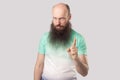 Portrait of serious bossy middle aged bald man with long beard in light green t-shirt standing with warning gesture and looking at