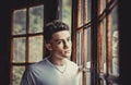 Portrait of serious boy teenager age looking on camera near cozy chalet wooden windows - concept of teen problems life indoor