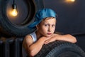 Portrait serious boy 7 years old, ileaning on the tire of a car in garage Royalty Free Stock Photo