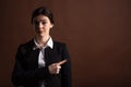 Portrait of serious brunette business woman pointing her finger to the side in studio on brown background with copyspace. Royalty Free Stock Photo
