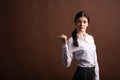 Portrait of serious brunette business woman pointing her thumb to the side in studio on brown background with copyspace. Royalty Free Stock Photo