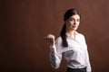 Portrait of serious brunette business woman pointing her thumb to the side in studio on brown background with copyspace. Royalty Free Stock Photo