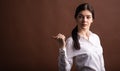 Portrait of serious brunette business woman pointing her thumb to the side in studio on brown background with copyspace. Royalty Free Stock Photo