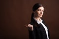 Portrait of serious brunette business woman pointing her thumb to the side in studio on brown background with copyspace. Royalty Free Stock Photo
