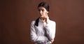 Portrait of a serious brunette business woman who thinks with her finger to her face in the studio on a brown background. Royalty Free Stock Photo