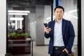 Portrait of serious concentrated businessman asian, man with phone in hands looking at camera, mature boss inside office Royalty Free Stock Photo