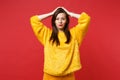 Portrait of serious confident young woman in yellow fur sweater putting hands on head isolated on bright red wall Royalty Free Stock Photo
