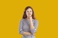 Confused young woman holding hand on chin thinking, trying to make hard choice on yellow background.