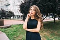 Portrait of serious elegante girl in the city park. She has long hair, black dress, vinous lips and looks wistfully Royalty Free Stock Photo