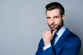 Portrait of serious fashionable handsome man in blue suit and tie touching chin and think Royalty Free Stock Photo