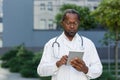 Portrait of serious and focused doctor at work, african american man in glasses working with tablet computer outside Royalty Free Stock Photo