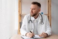 Portrait of a serious general practitioner in a white medical uniform sitting at a table in a hospital, a doctor or Royalty Free Stock Photo