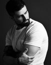 Portrait of serious handsome bearded brutal muscular man with tattoo on hands in white t-shirt embracing hands and looking aside