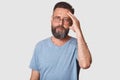 Portrait of serious handsome male with beard and mustache, keeps hand on forhead, wearing grey t shirt, posing isolated over white Royalty Free Stock Photo