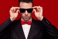 Portrait of serious handsome stylish man in elegant black suit and sunglasses on red background Royalty Free Stock Photo