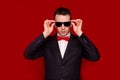 Portrait of serious handsome stylish man in elegant black suit and sunglasses on red background Royalty Free Stock Photo