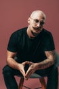 Portrait of serious hipster bald bearded man with moustache in glasses who sitting on chair Royalty Free Stock Photo