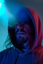 Portrait of serious man in hoodie and sunglasses against blue studio background in neon light. Night life Royalty Free Stock Photo