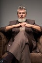 Portrait of serious mature businessman with beard wearing elegant suit looking at camera, sitting with hands crossed in Royalty Free Stock Photo