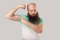 Portrait of serious middle aged bald man with long beard in light green t-shirt standing, pointing his bicep and looking at with