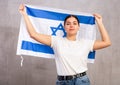 Portrait of serious young female holding national flag of Israel against gray wall