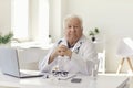 Serious senior physician sitting at desk with laptop in hospital office looking at camera