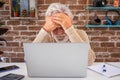 Portrait of serious senior man using laptop computer in home office. Brick wall in background Royalty Free Stock Photo