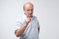 Portrait of serious senior man with warning finger and blue shirt shirt against light gray background. Royalty Free Stock Photo